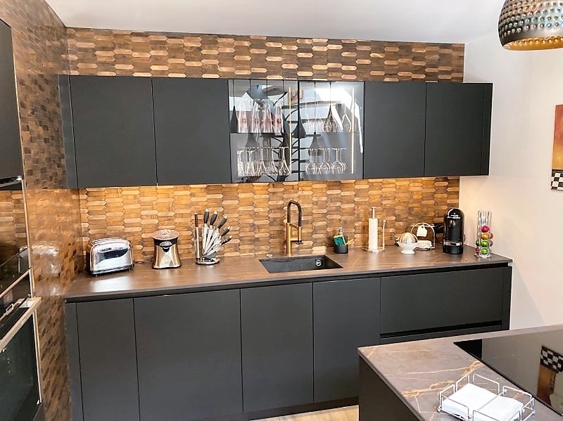 Projet réalisé par Cuisines de l’Erdre à Carquefou : une cuisine contemporaine ARMONY CUCINE avec façades laquées noires, plan de travail en céramique Dekton Laurent et vitrines rétroéclairées